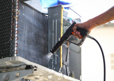 Technician cleaning air conditioner with water spray.