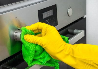 Hand in glove with green rag is wiping oven in kitchen